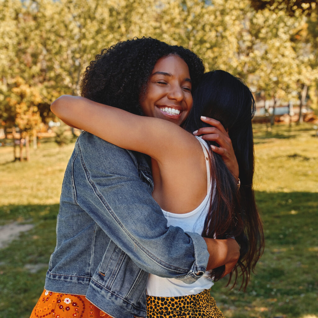 Two happy diverse female friends hugging in the park on a sunny day