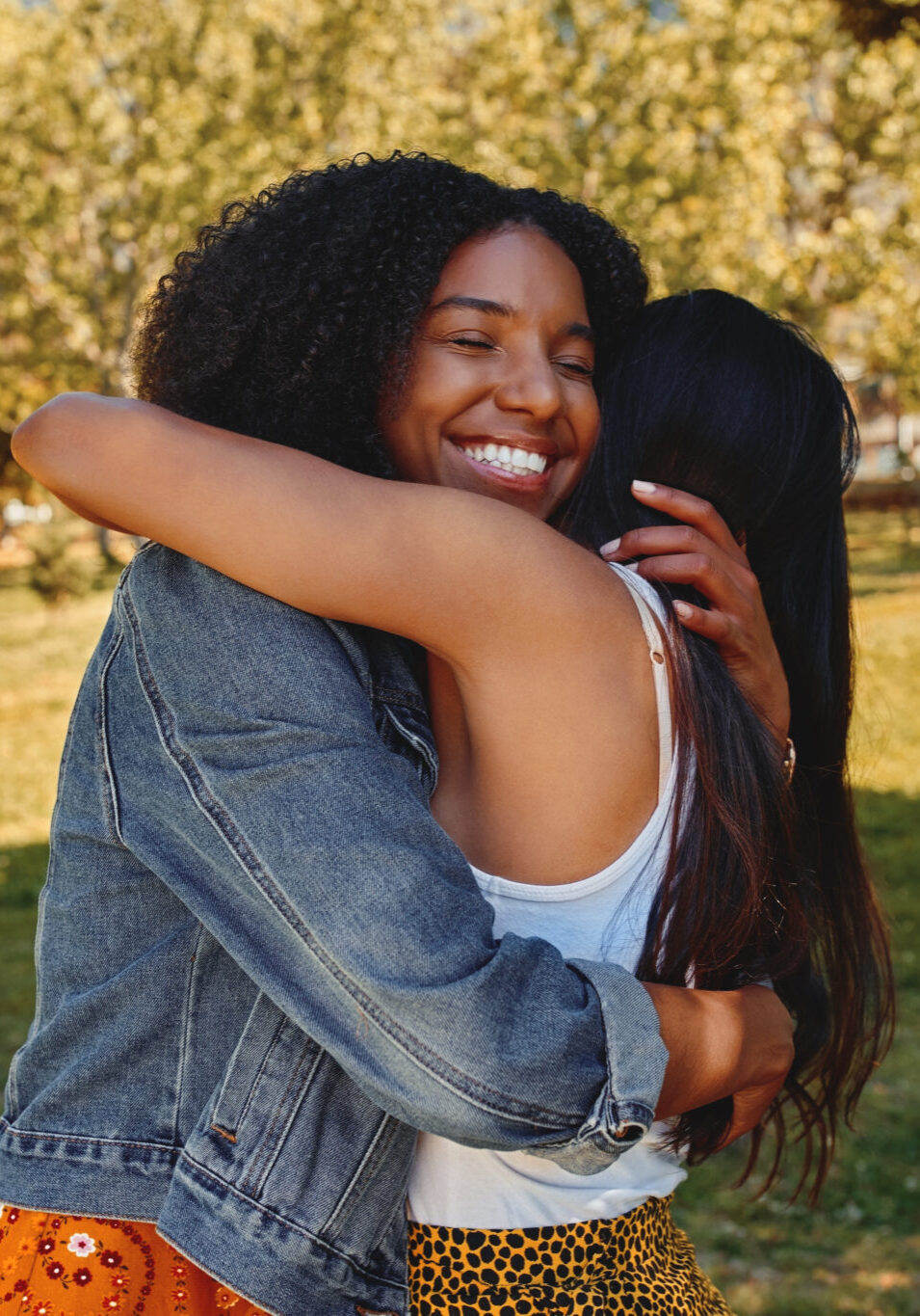 Two happy affectionate diverse young women friends hugging each other in the park - two friends hugging each other outdoors Two happy diverse female friends hugging in the park on a sunny day