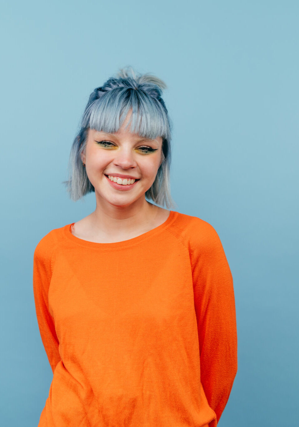 Smiling hipster girl with colored hair stands on a blue background with a happy face and looks at the camera. Smiling hipster girl with colored hair stands on a blue background with a happy face and looks at the camera.